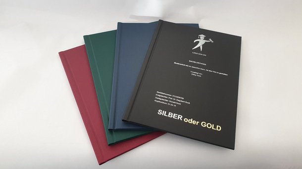 Abschlussarbeit Hardcover unbedrucktes Cover: Vier Hardcover-Bücher liegen versetzt übereinander. Die Einbände sind in Dunkelrot, Dunkelgrün, Dunkelblau und Schwarz gehalten. Das vordere, schwarze Buch hat einen goldfarbenen Aufdruck, in Wiesbaden bei City Medien Einkaufswelt für Partner