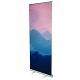 Roll Up Budget B 60 cm x H 160 cm: Ein hochformatiges Roll-Up-Display mit einem bedruckten Banner. Das Banner zeigt ein abstraktes Motiv von Bergen in den Farben Rosa und Blau. Das Display hat eine silberne Kassette mit zwei ausklappbaren Füßen, in Wiesbaden bei City Medien Einkaufswelt für Partner