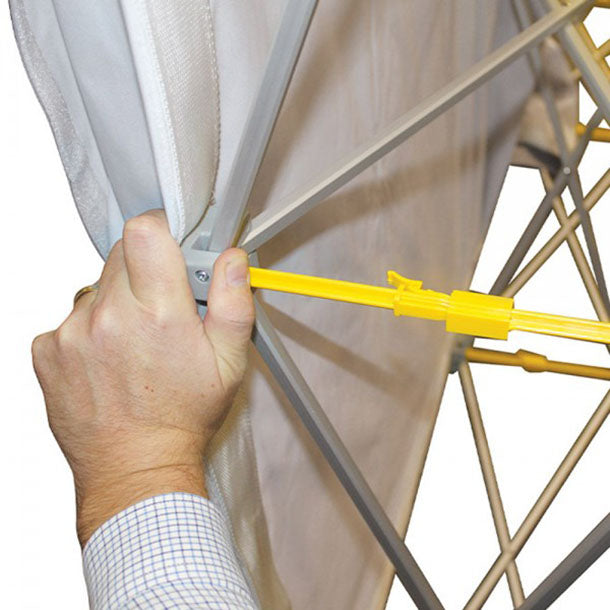 Textilfalttheke B 106 cm x H 102 x T 36 cm: Eine Hand befestigt eine weiße Stoffbespannung mit einer gelben, länglichen Plastikschiene am Thekengestell. Die Hand hält eine graue Stange des Gestells fest, in Wiesbaden bei City Medien Einkaufswelt für Partner