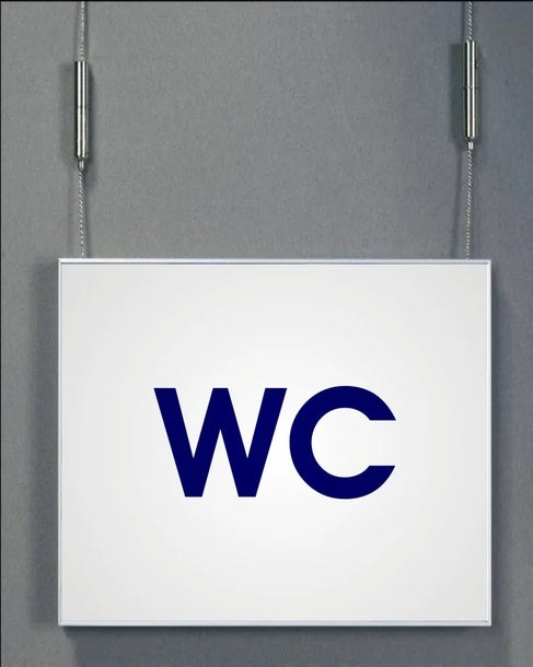 Deckenhänger System Karlsruhe: Ein rechteckiges Schild mit einem silbernen Aluminiumrahmen. Auf dem Schild steht in blauer Schrift „WC“ geschrieben. Das Schild hängt an zwei silbernen Drahtseilen von der Decke, in Wiesbaden bei City Medien Einkaufswelt für Partner