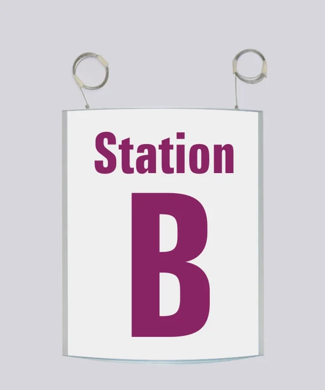 Deckenhänger System Zenit: Ein rechteckiges Schild. Auf dem Schild steht in magentafarbener Schrift „Station B“. Das Schild hängt an zwei silbernen Drahtseilen von der Decke, in Wiesbaden bei City Medien Einkaufswelt für Partner
