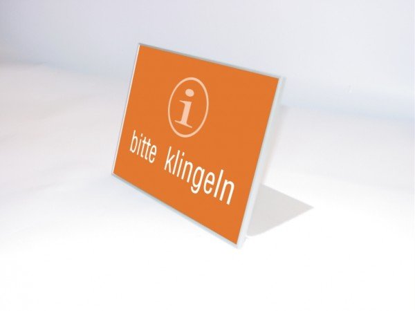 Tischaufsteller System Karlsruhe: Ein silberner Tischaufsteller mit einem rechteckigen, orangenen bedruckten Blatt. Der Druck hat einen weißen Kreis mit einem „i“ und den weißen Schriftzug „bitte klingeln“, in Wiesbaden bei City Medien Einkaufswelt für Partner