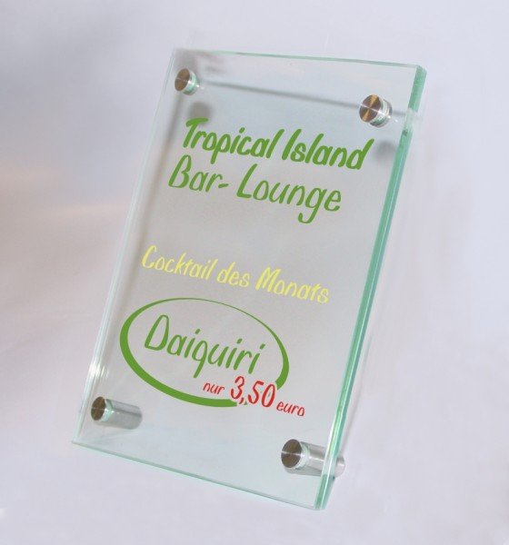 Tischaufsteller System Seeshaupt: Ein rechteckiger Tischaufsteller aus zwei klaren Acrylglasscheiben. Der Druck zwischen den Scheiben zeigt die Aufschrift „Tropical Island Bar-Lounge“ in grüner und „Daiquiri“ in grüner und roter Schrift. In der Mitte steht der gelbe Schriftzug „Cocktail des Monats“. Der Aufsteller wird von vier silbernen Metallstiften zusammengehalten, in Wiesbaden bei City Medien Einkaufswelt für Partner