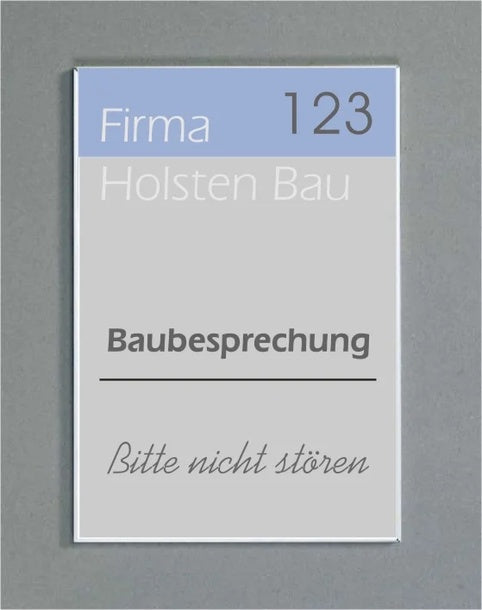 Wandschild System Karlsruhe: Ein rechteckiges Schild mit einem silbernen Rahmen. Es ist dreigeteilt in einen hellblauen Bereich mit der Aufschrift „Firma 123“, einen hellgrauen Bereich mit „Holsten Bau“ und einen weißen Bereich mit dem Text „Baubesprechung“ und „Bitte nicht stören“. Das Schild ist an einer grauen Wand befestigt, in Wiesbaden bei City Medien Einkaufswelt für Partner