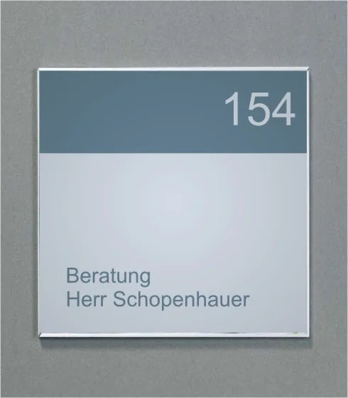 Wandschild System Karlsruhe: Ein quadratisches Schild mit einem silbernen Rahmen. Der obere Bereich ist dunkelgrau mit der weißen Zahl „154“. Der untere Bereich ist hellgrau mit dem grauen Text „Beratung Herr Schopenhauer“. Das Schild ist an einer grauen Wand befestigt, in Wiesbaden bei City Medien Einkaufswelt für Partner