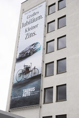 Mesh Banner – einseitig bedruckt, hochformatiges Netzbanner mit Werbedruck an mehrstöckigem Gebäude, windstabil und wetterfest in Wiesbaden von City Medien Einkaufswelt für Partner günstig kaufen, drucken lassen, online preiswert bestellen – Mesh Banner, Fassadenbanner, Großflächenwerbung