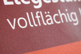 Liegestuhl mit Armlehne: Nahaufnahme des braun-roten Stoffsitzes. Der Stoff hat eine sichtbare Textur. Es ist ein weißer, vollflächiger Druck zu sehen, in Wiesbaden bei City Medien Einkaufswelt für Partner