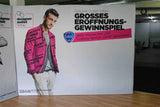 Textilfaltwand: Eine gerade Textilfaltwand mit einem Werbedruck für das „Designer Outlet Soltau“. Der Druck zeigt einen Mann in einem pinken Anzug, in Wiesbaden bei City Medien Einkaufswelt für Partner