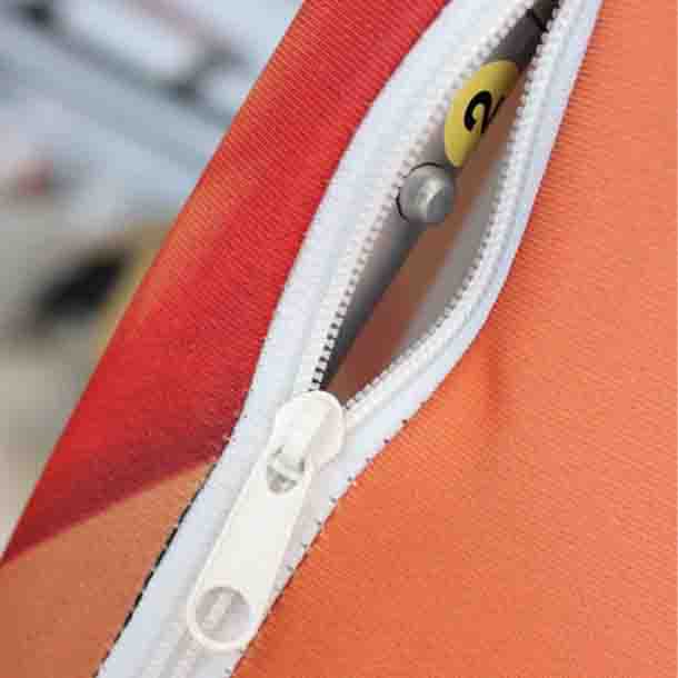 Textilwand ALU gerade gebogen: Nahaufnahme des oberen Endes der Textilbespannung. Die Bespannung ist orange-rot mit einem weißen Reißverschluss, in dem die silberne Stange mit einem gelben Aufkleber sichtbar ist, in Wiesbaden bei City Medien Einkaufswelt für Partner