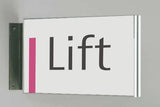 Fahnenschild System Seeshaupt: Ein querformatiges, weißes Schild mit silbernem Rahmen. An der linken Seite befindet sich ein vertikaler, rosafarbener Streifen. In der Mitte steht das Wort „Lift“ in grauer Schrift. Das Schild ist an einer schwarzen Halterung an der Wand montiert, in Wiesbaden bei City Medien Einkaufswelt für Partner