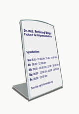 Tischaufsteller System Zenit: Ein silberner Tischaufsteller mit einem geschwungenen oberen Rand. Er zeigt ein bedrucktes Papier mit den blauen Aufschriften „Dr. med. Ferdinand Binger“, „Facharzt für Allgemeinmedizin“ und den Sprechzeiten, in Wiesbaden bei City Medien Einkaufswelt für Partner