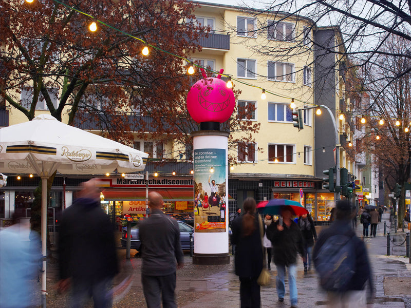 Hüpfball-Sonderbau auf Litfaßsäule vor Einkaufsstraße, Lichterkette & Passanten – 3D-Werbung Out-of-Home, City Medien Einkaufswelt für Partner Wiesbaden – Kategorien: Sonderproduktion, Aufblasbare Werbung – anfragen, produzieren lassen, bestellen