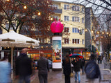 Hüpfball-Sonderbau auf Litfaßsäule vor Einkaufsstraße, Lichterkette & Passanten – 3D-Werbung Out-of-Home, City Medien Einkaufswelt für Partner Wiesbaden – Kategorien: Sonderproduktion, Aufblasbare Werbung – anfragen, produzieren lassen, bestellen